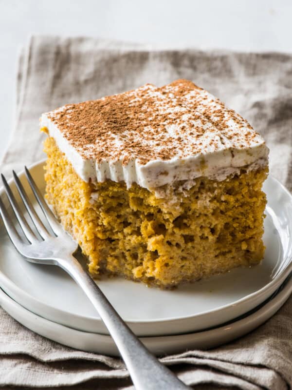 A slice of pumpkin tres leches cake topped with whipped cream and garnished with a dusting of pumpkin spice seasoning.