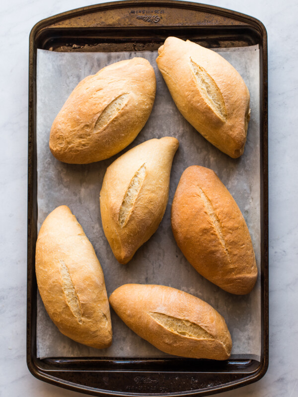 Six bolillo breads on a baking sheet ready to eat.