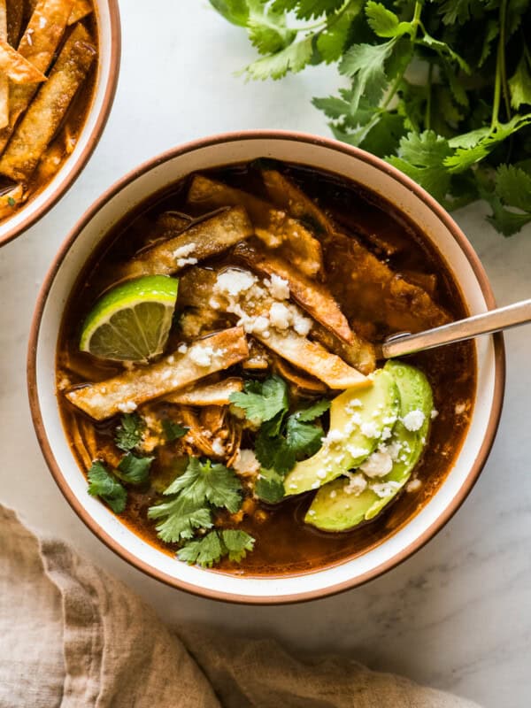 Chicken tortilla soup in a bowl topped with tortilla strips, cilantro, avocado, and queso fresco.