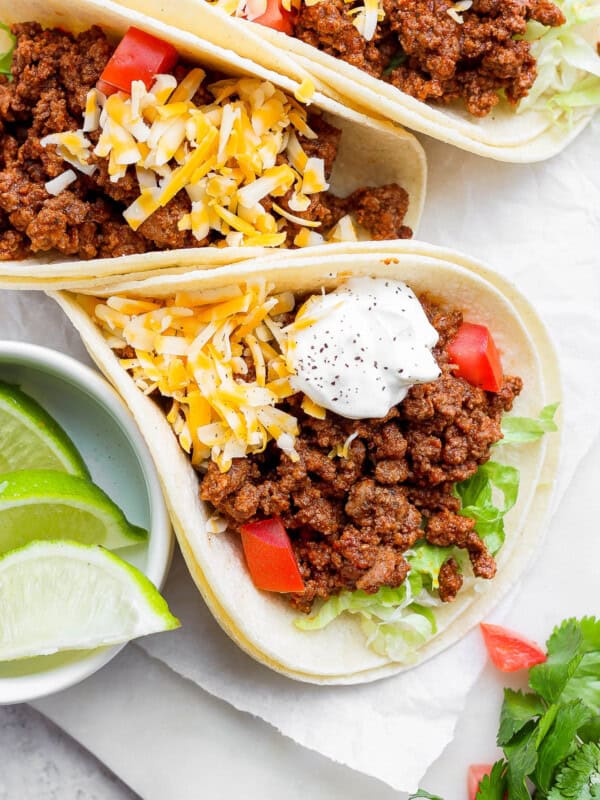 Ground beef tacos topped with shredded cheese, sour cream, and diced tomatoes.