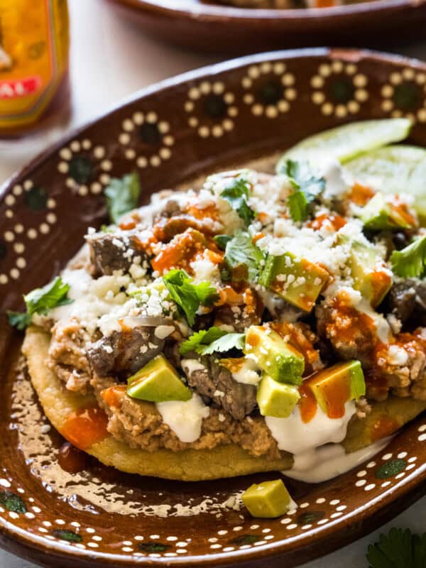 Mexican Huaraches on a plate topped with refried beans, cheese, and more.