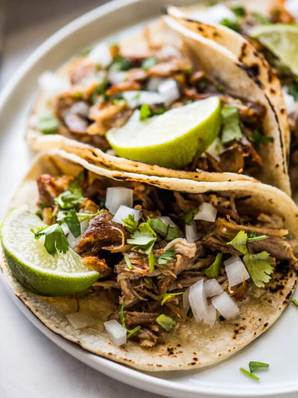 Carnitas (Mexican slow cooked pulled pork) in a corn tortilla topped with onion, cilantro, and lime.