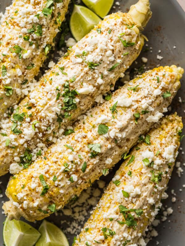 Elotes (Mexican Street Corn) on a plate with cotija cheese, cilantro, and mayo.