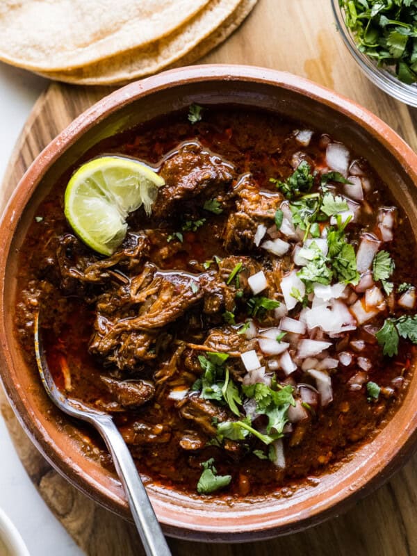 A bowl of beef birria topped with chopped cilantro, onions, and a lime wedge.