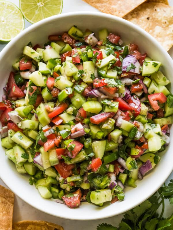 Cucumber Salsa in a bowl with tortilla chips, lime wedges, and cilantro on the side.