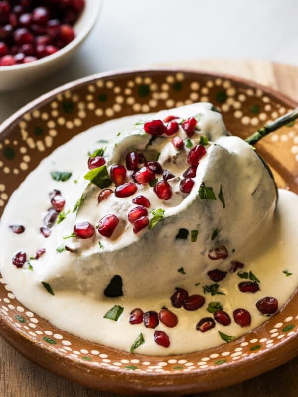 A chile en nogada on a plate garnished with pomegranate seeds and parsley.