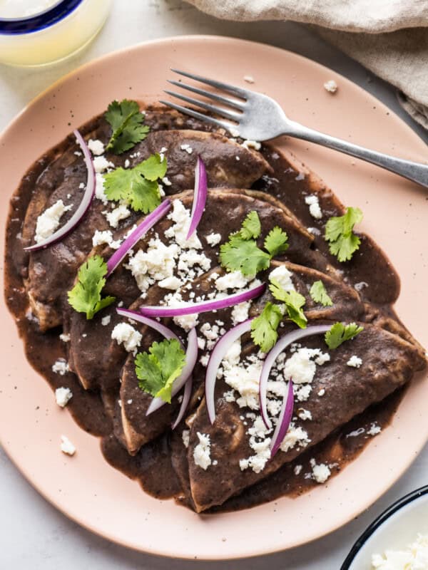 Enfrijoladas covered in a blended bean sauce and garnished with queso fresco, cilantro, and sliced onions.