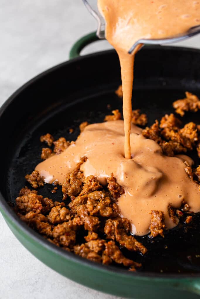 Blended pinto beans being poured in a skillet with chorizo.