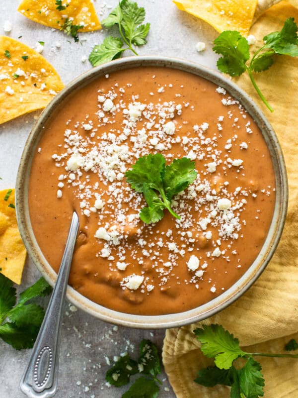 Frijoles puercos in a bowl topped with cotija cheese and served with tortilla chips.