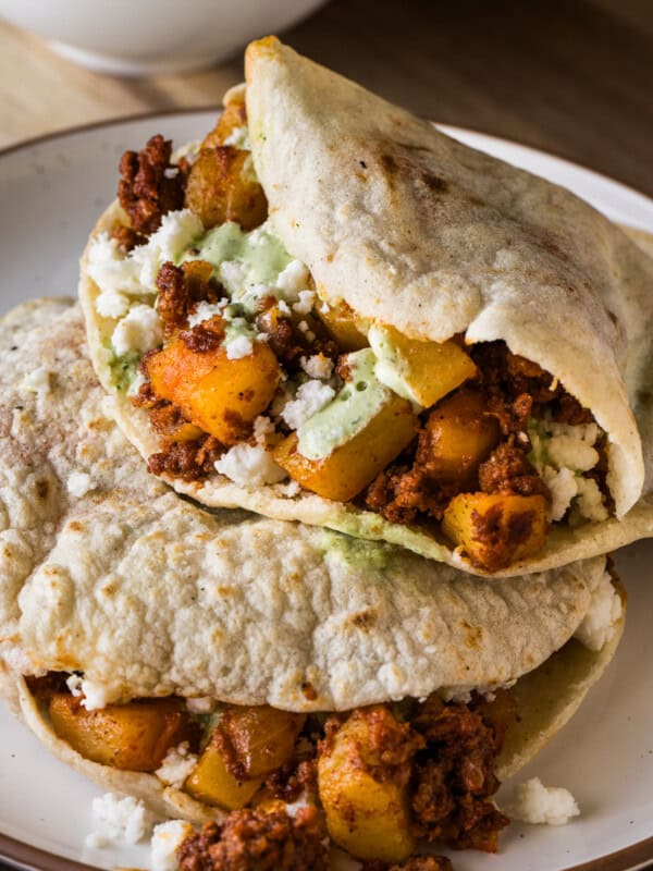 Gorditas stacked on top of one another filled with papas con chorizo and garnished with queso fresco and cilantro lime crema.