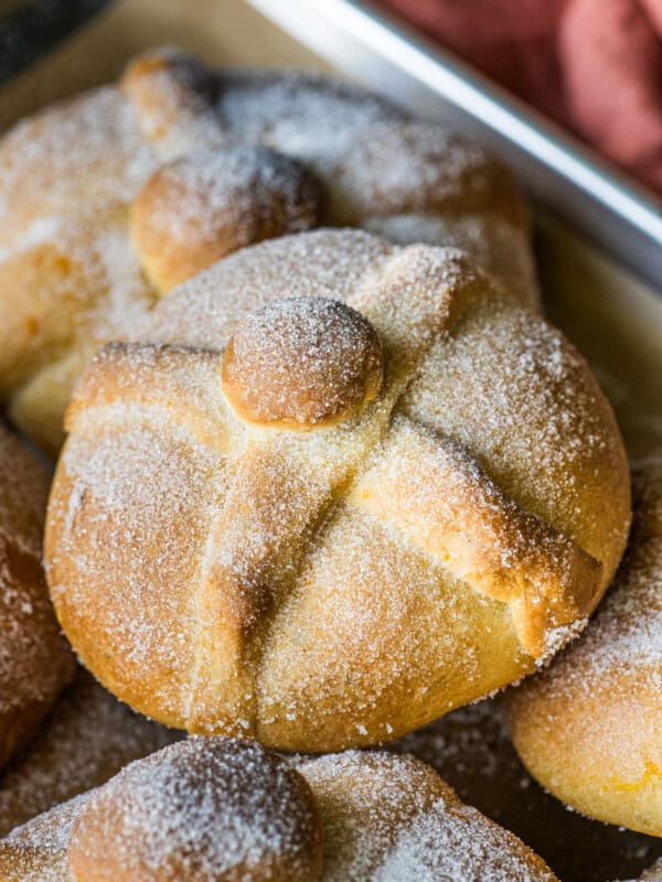 Pan de Muerto on a baking sheet rolled in cinnamon.