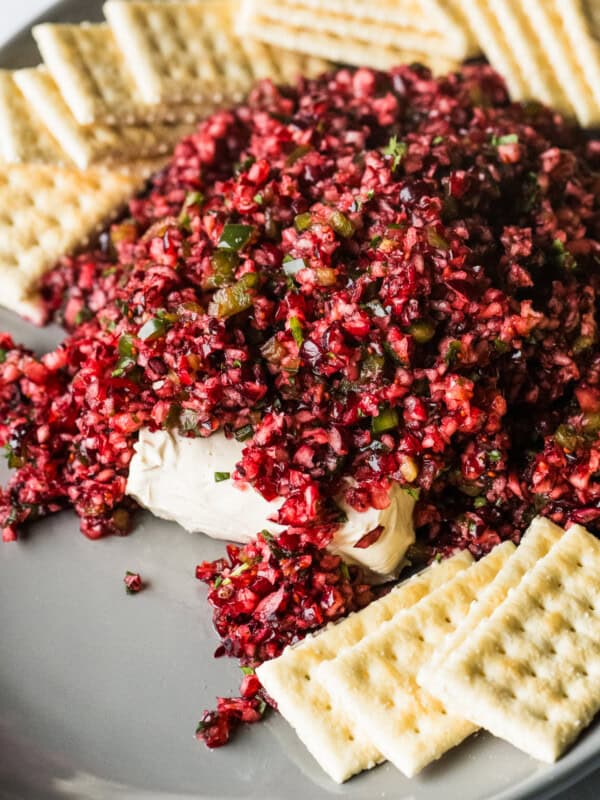 Cranberry salsa on a serving plate on top of a block of cream cheese with some crackers on the side.