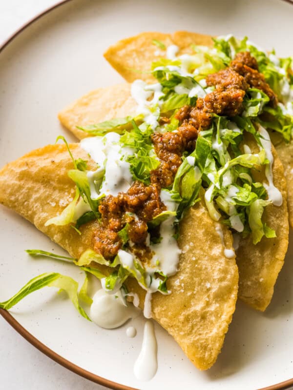 Fried quesadillas (quesadillas fritas) on a plate topped with lettuce, salsa, and Mexican crema.