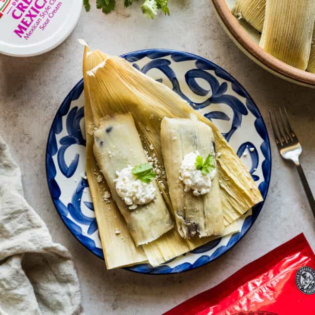 Black bean and cheese tamales garnished with crema and cotija cheese.