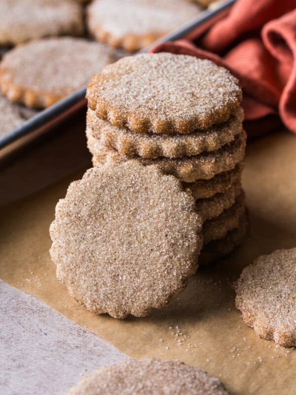 Biscochitos covered in cinnamon sugar stacked on top of one another on a piece of parchment paper.