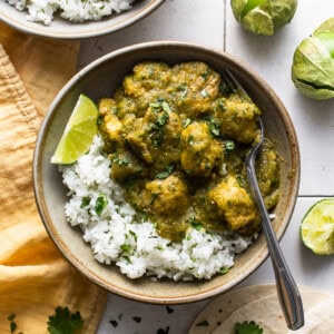 Chile verde in a bowl served on top of some cilantro lime rice, fresh cilantro, and lime wedges.