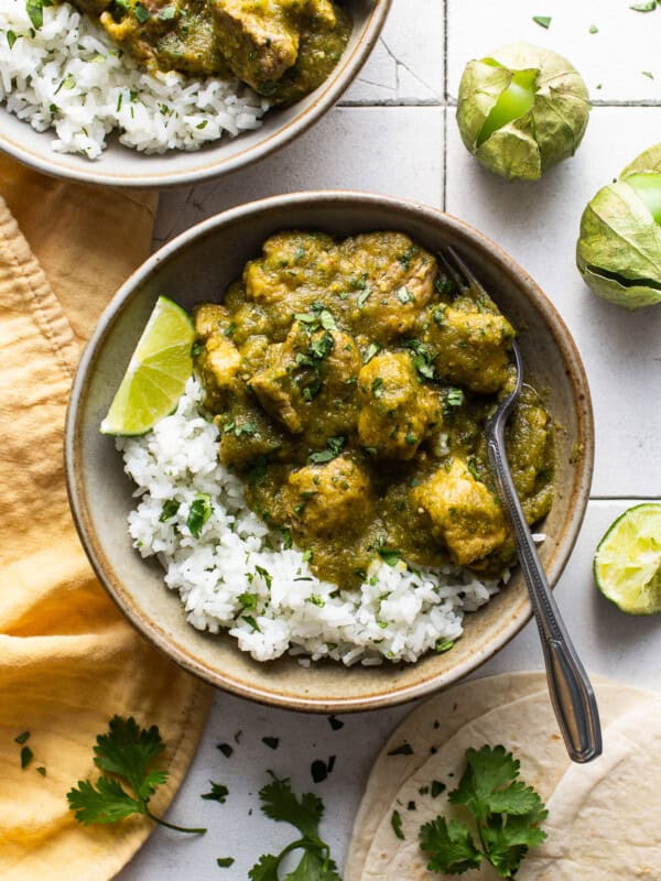 Chile verde in a bowl served on top of some cilantro lime rice, fresh cilantro, and lime wedges.