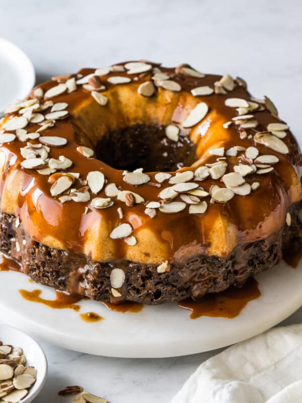 Chocoflan topped with cajeta and sliced almonds on a cake stand.