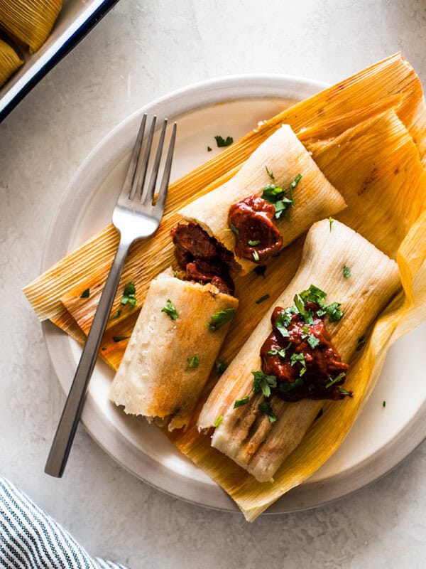 Learn how to make tamales right at home with these simple step-by-step instructions! This authentic Mexican tamales recipe is filled with tender pieces of pork simmered in a delicious red chile sauce wrapped in a soft and fluffy masa dough.