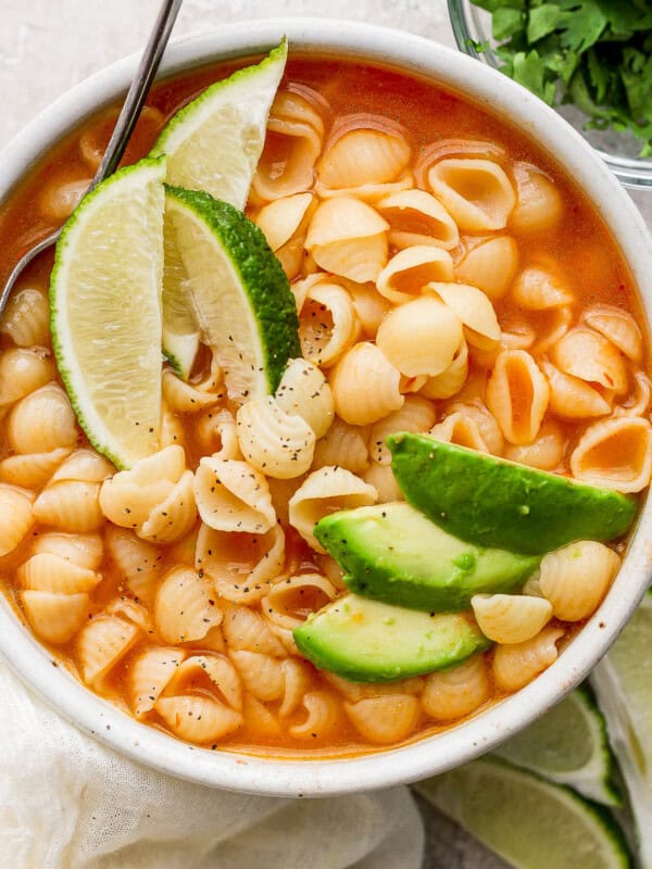 Sopa de conchas in a white bowl topped with sliced avocado.