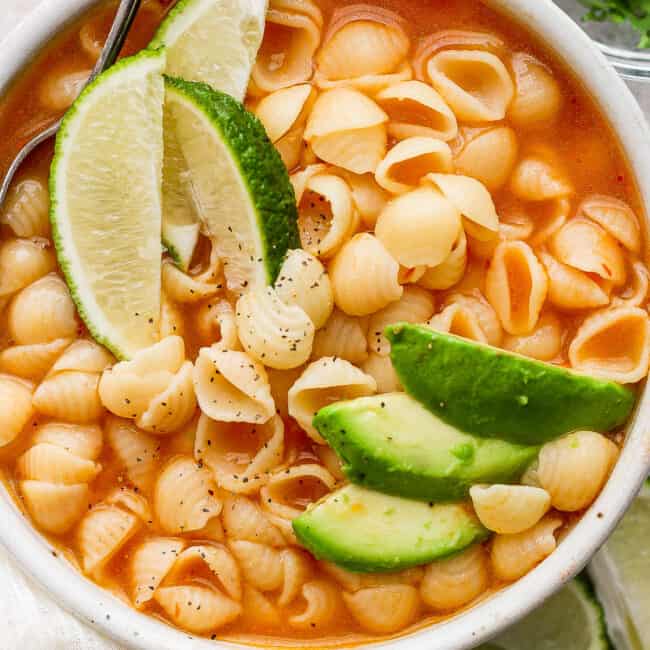 Sopa de conchas in a white bowl topped with sliced avocado.