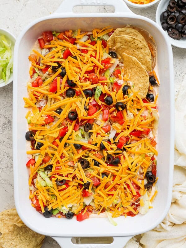 Taco dip in a baking dish topped with shredded cheese, tomatoes, and olive served with tortilla chips.