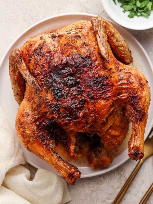 Air fryer whole chicken on a plate with crispy golden skin ready to eat.