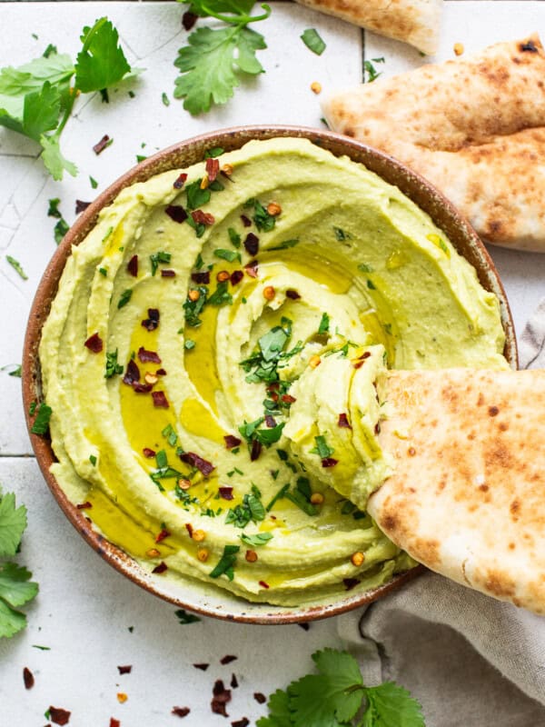 A slice of pita bread being dipped in a bowl of avocado hummus.