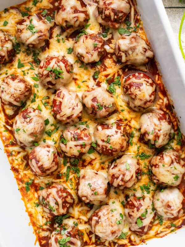 Enchilada meatballs baked in dish topped with cheese, cilantro, and enchilada sauce.