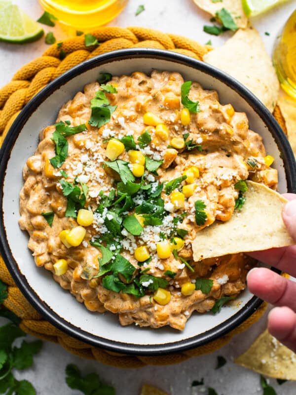 A bowl of Mexican corn dip with a tortilla chip being dipped inside.