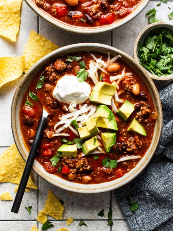 Chorizo chili in a bowl topped with shredded cheese, avocado, sour cream, and served with tortilla chips.