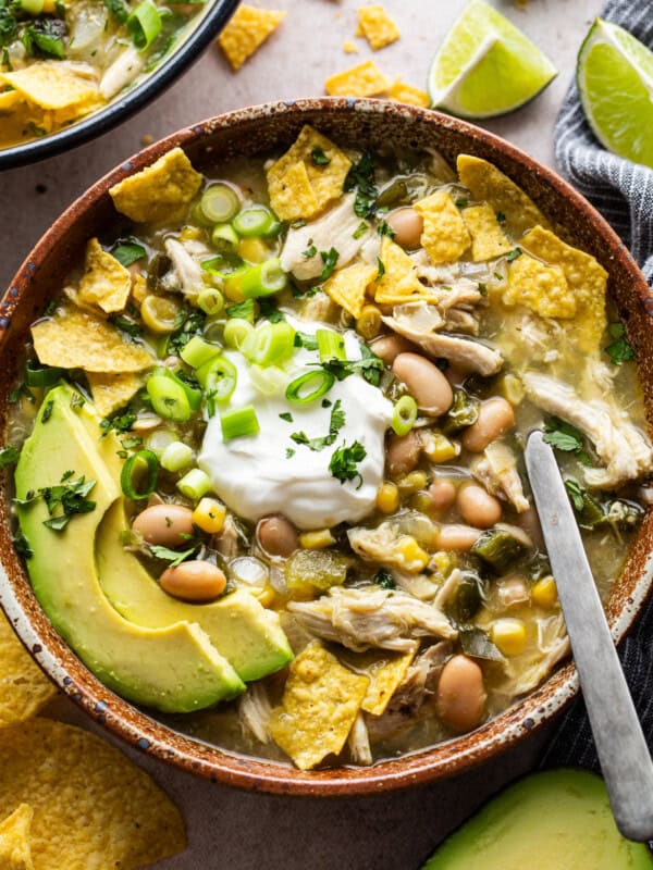 Green chicken chili in a bowl garnished with sour cream, tortilla chips, avocado, cilantro, and green onions.