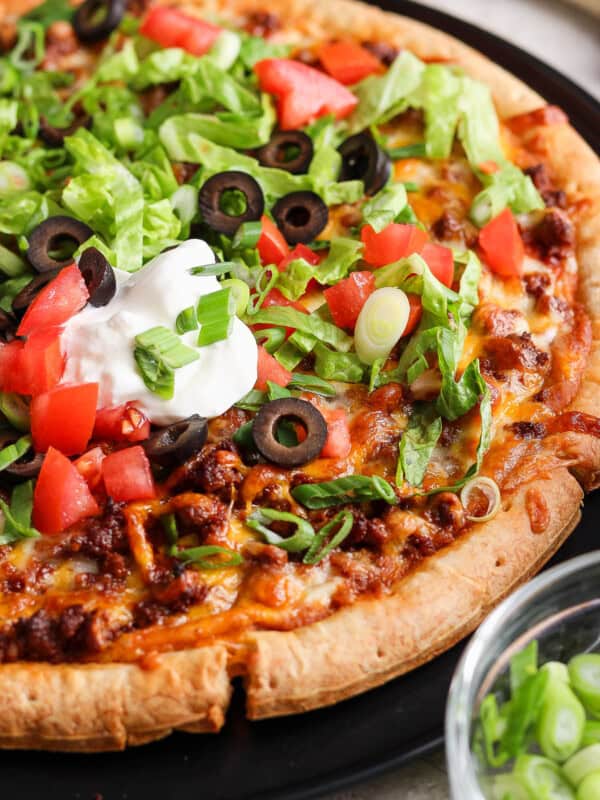 Taco pizza topped with shredded lettuce, sour cream, diced tomatoes, and olives.