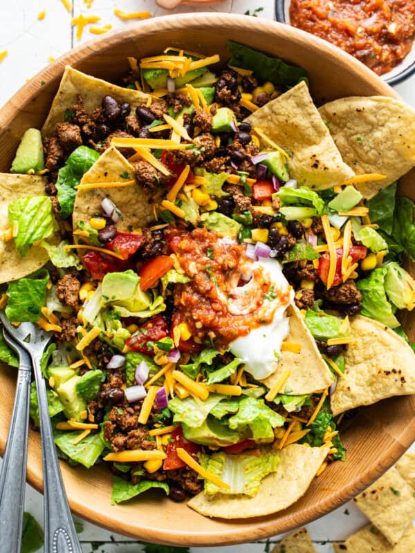 A big bowl of taco salad with ground beef, cheese, lettuce, beans, sour cream, salsa, and tortilla chips.