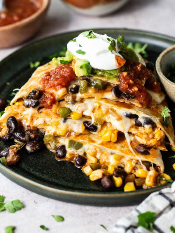 Black bean quesadillas on a plate with sour cream, guacamole, and salsa.