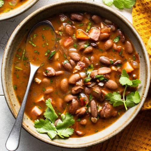 A bowl of charro beans topped with fresh cilantro on a table.