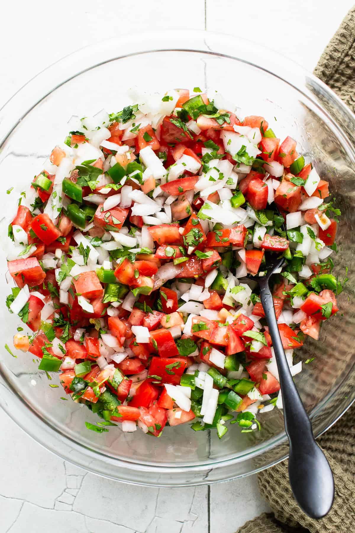 Pico de gallo ingredients tossed together in a glass bowl.
