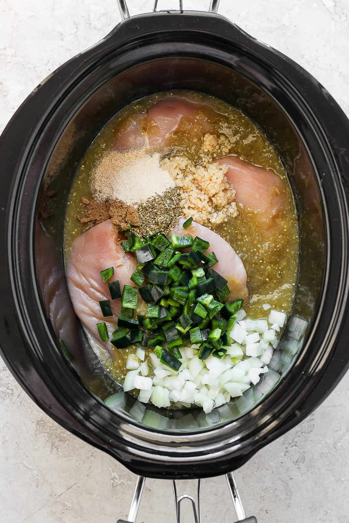 Raw chicken added to crockpot with salsa verde, seasonings, poblano peppers, and onions