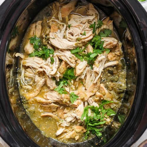 Salsa verde chicken in a slow cooker crock pot with fresh cilantro.