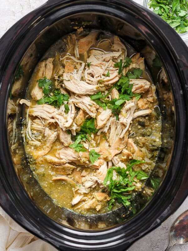 Salsa verde chicken in a slow cooker crock pot with fresh cilantro.