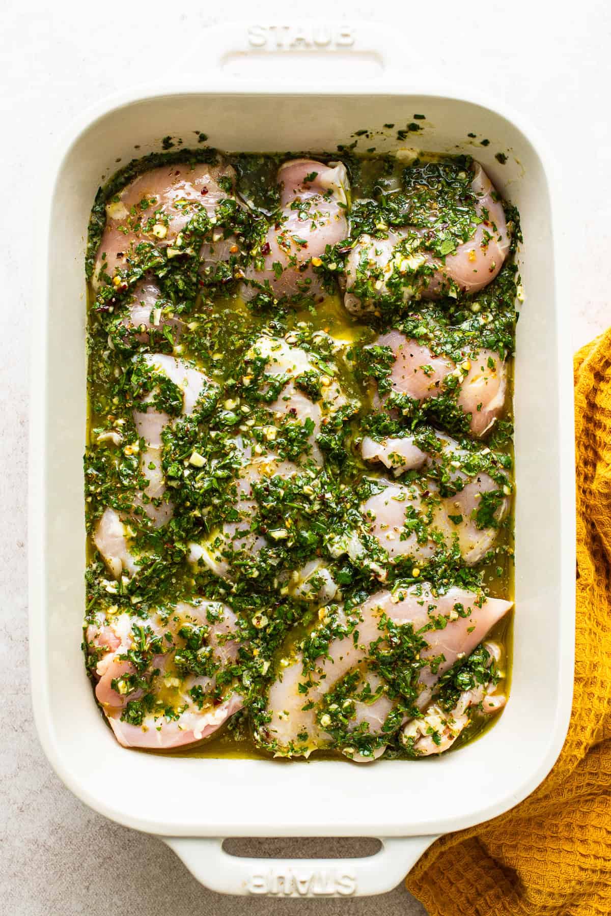 Chicken thighs in a dish covered in the chimichurri sauce ready to marinate
