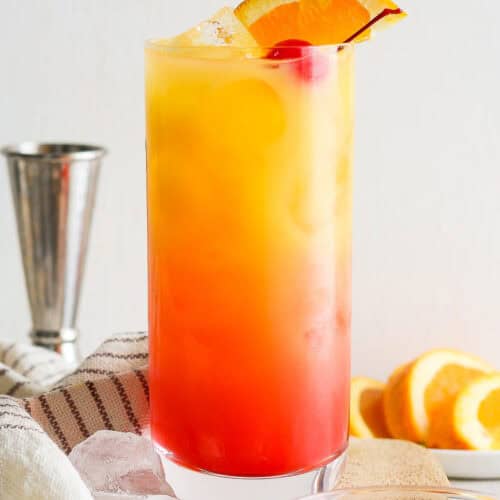 Tequila sunrise on a table garnished with an orange slice and maraschino cherry.