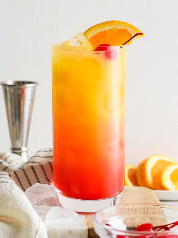 Tequila sunrise on a table garnished with an orange slice and maraschino cherry.