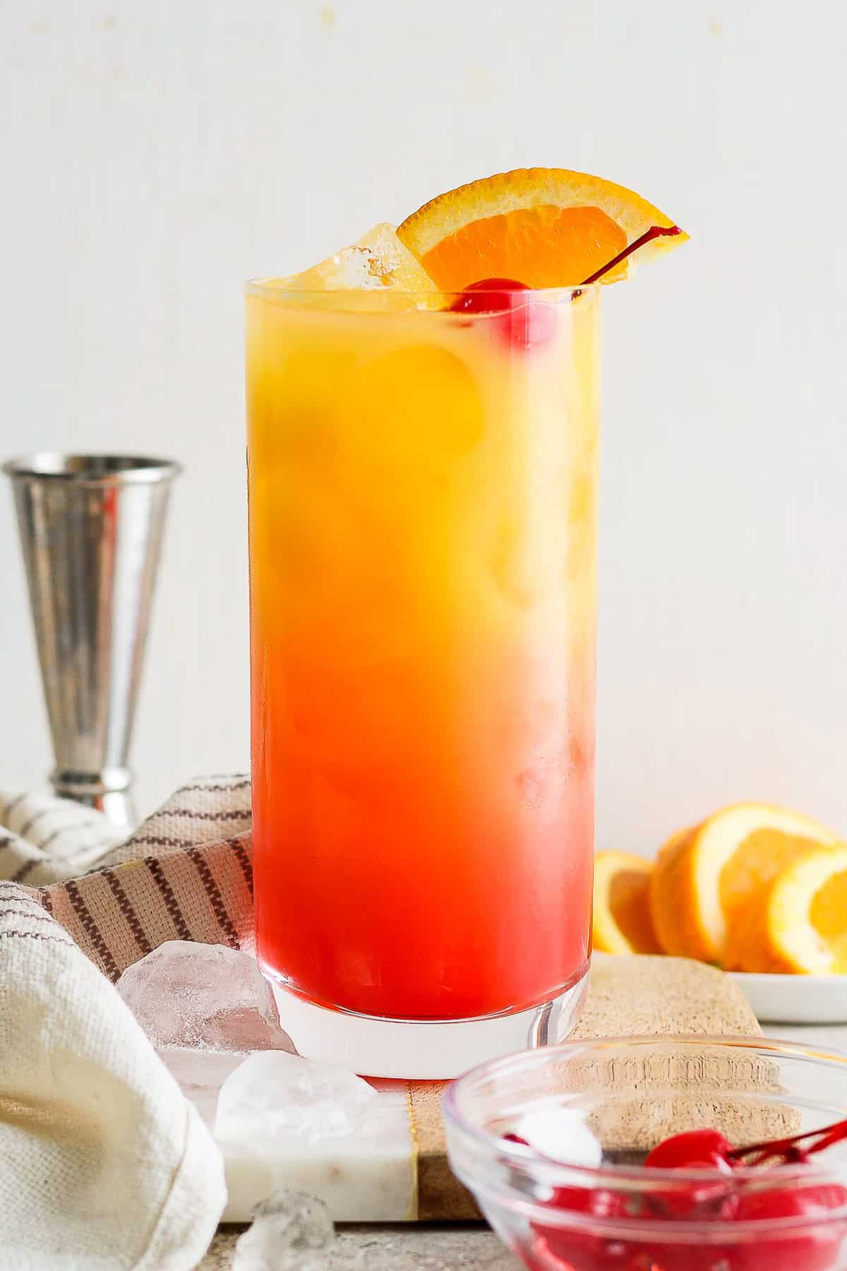 Tequila sunrise on a table garnished with an orange slice and maraschino cherry.