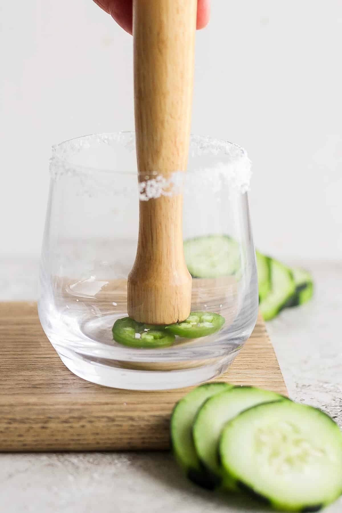 Jalapeño slices being muddled in a glass.
