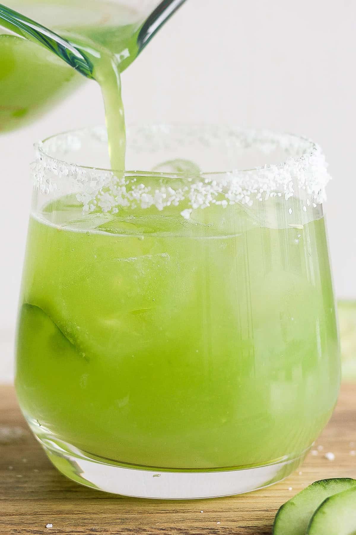 An iced glass with a cucumber margarita being poured in it.