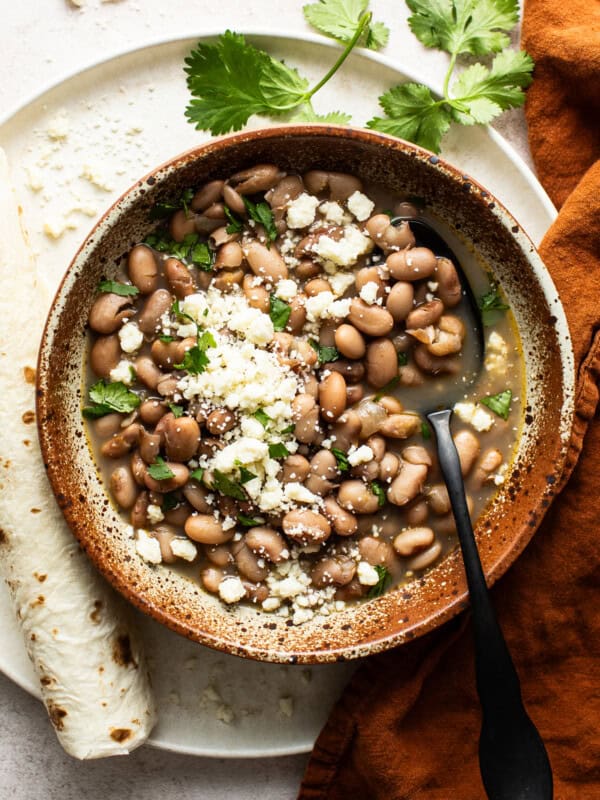 Cooked pinto beans in a bowl topped with cilantro, cotija cheese, and served with flour tortillas