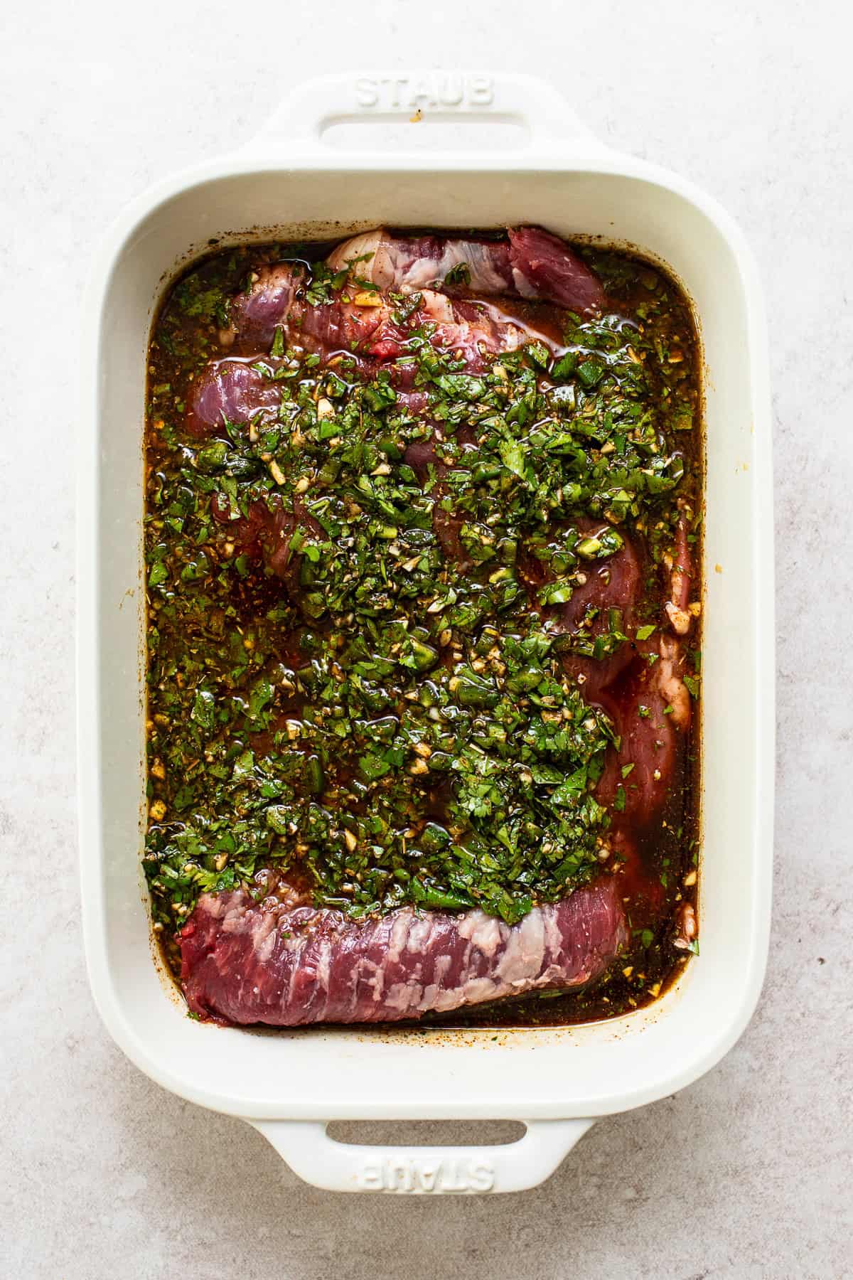 Carne asada steak being marinaded in a baking dish.