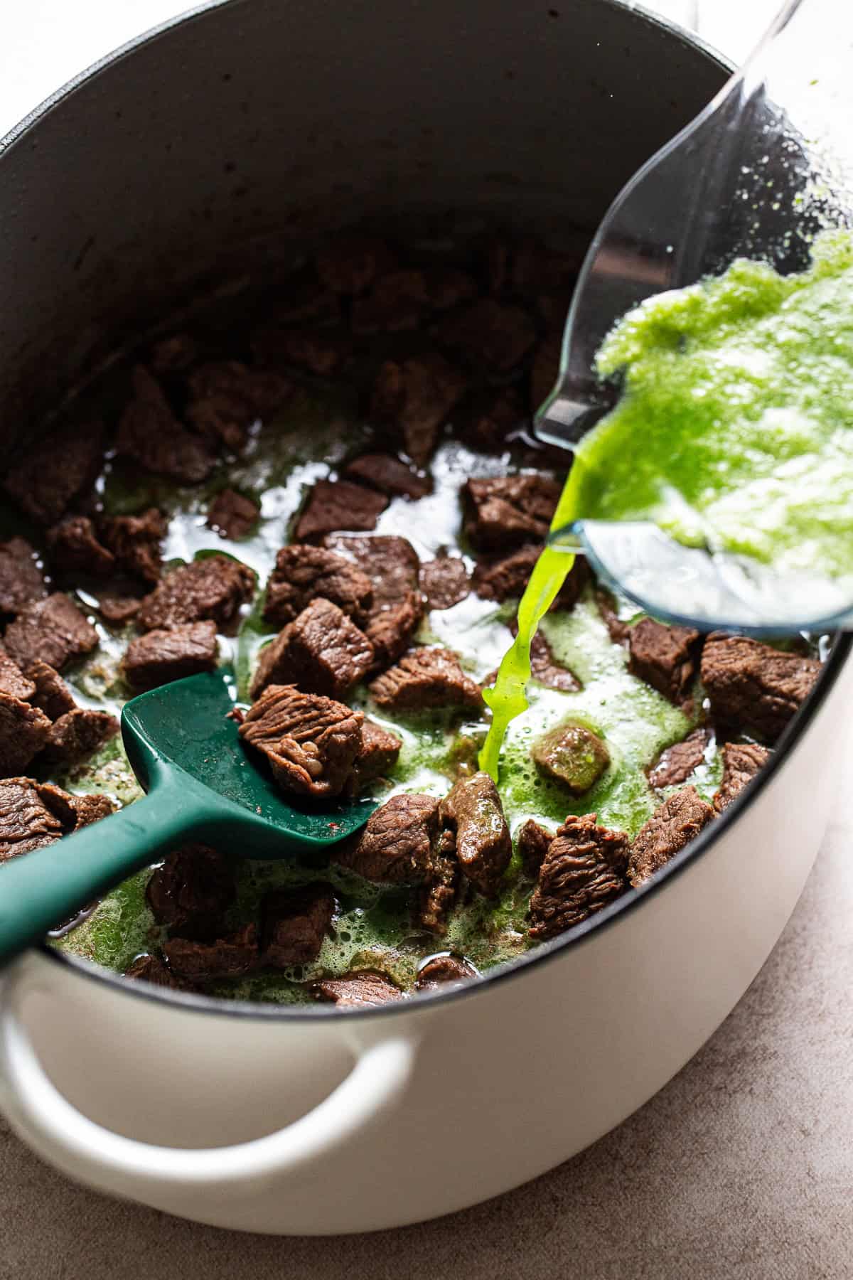 Tomatillo sauce is being poured into the browned beef pot.