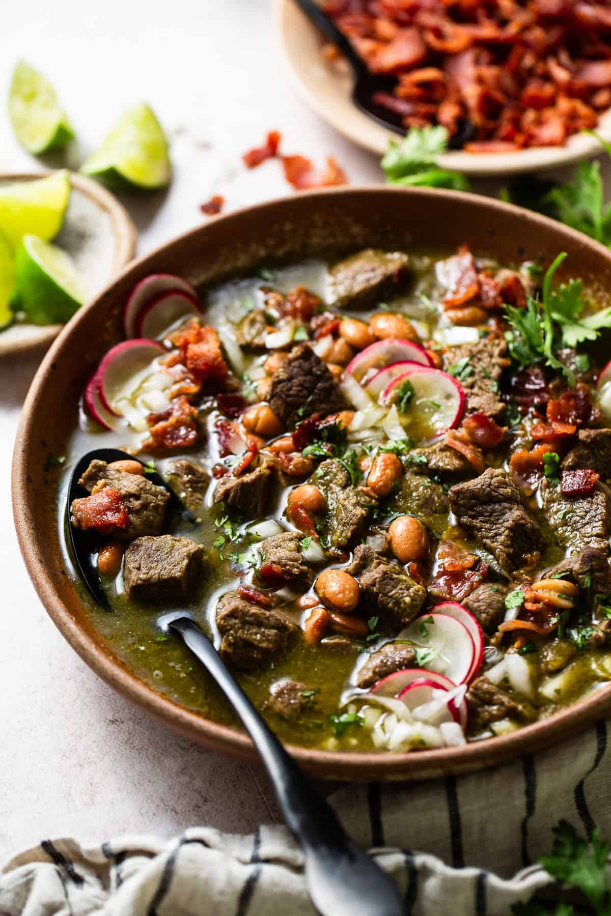 Carne en su Jugo served in bowls and garnished with cilantro, onion, and radishes.